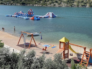 A beach with inflatable play structures, a swing set, and a small boat. - Apartments Glorija (Rogoznica)