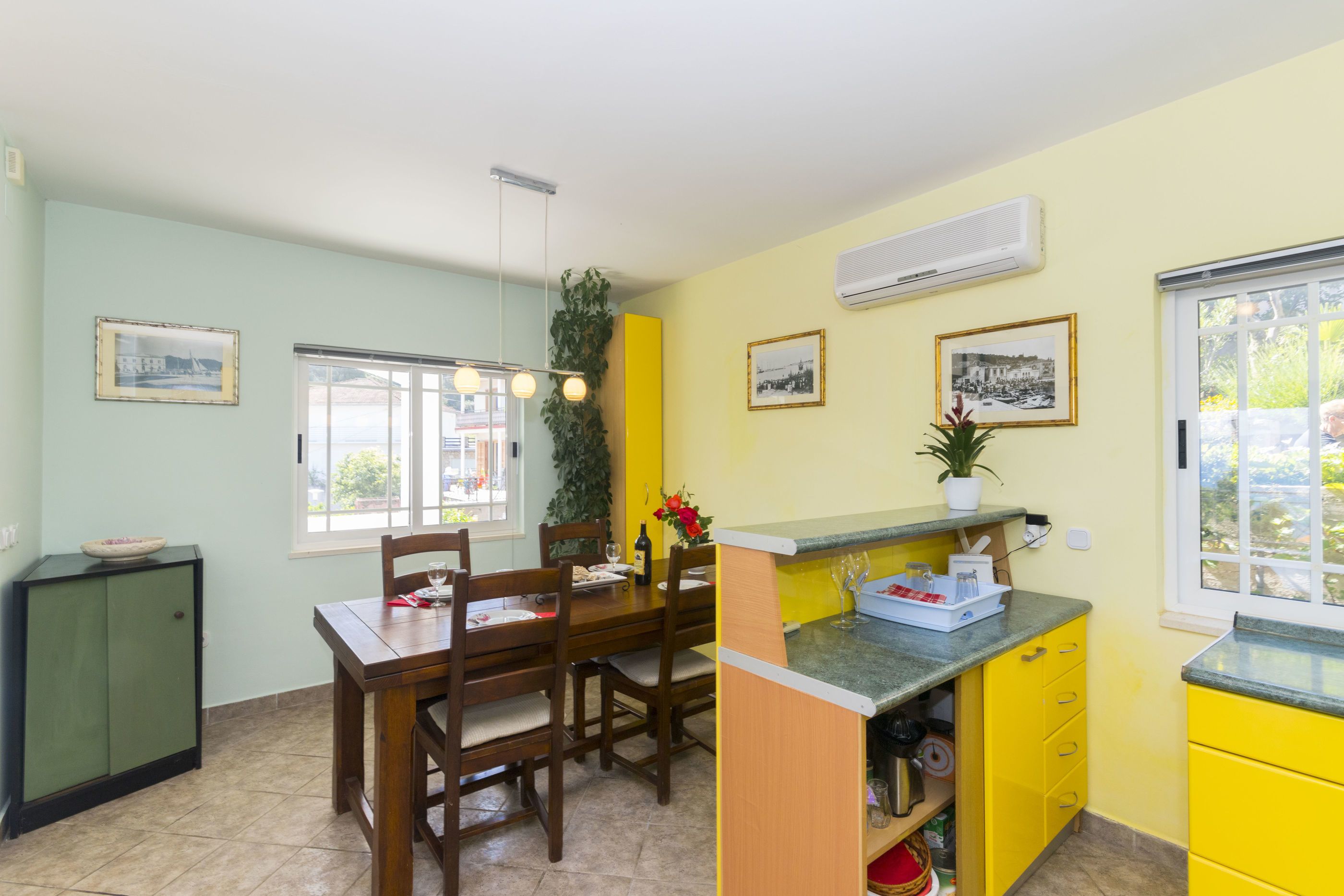 A dining area with a wooden table and chairs, a small kitchen counter, and a window with a view.