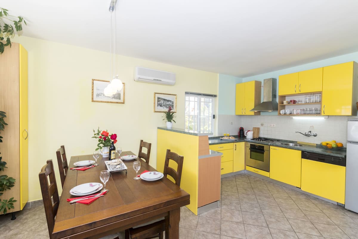 Une cuisine avec des meubles de rangement jaunes, une table à manger en bois et une fenêtre.