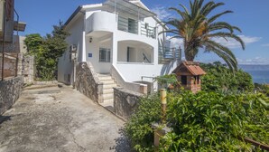Un edificio blanco de dos pisos con un balcón, una escalera que conduce a la entrada y vista al mar.