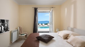 Ein Hotelzimmer mit Bett, Sessel, Heizkörper und Blick auf Pool und Berge.