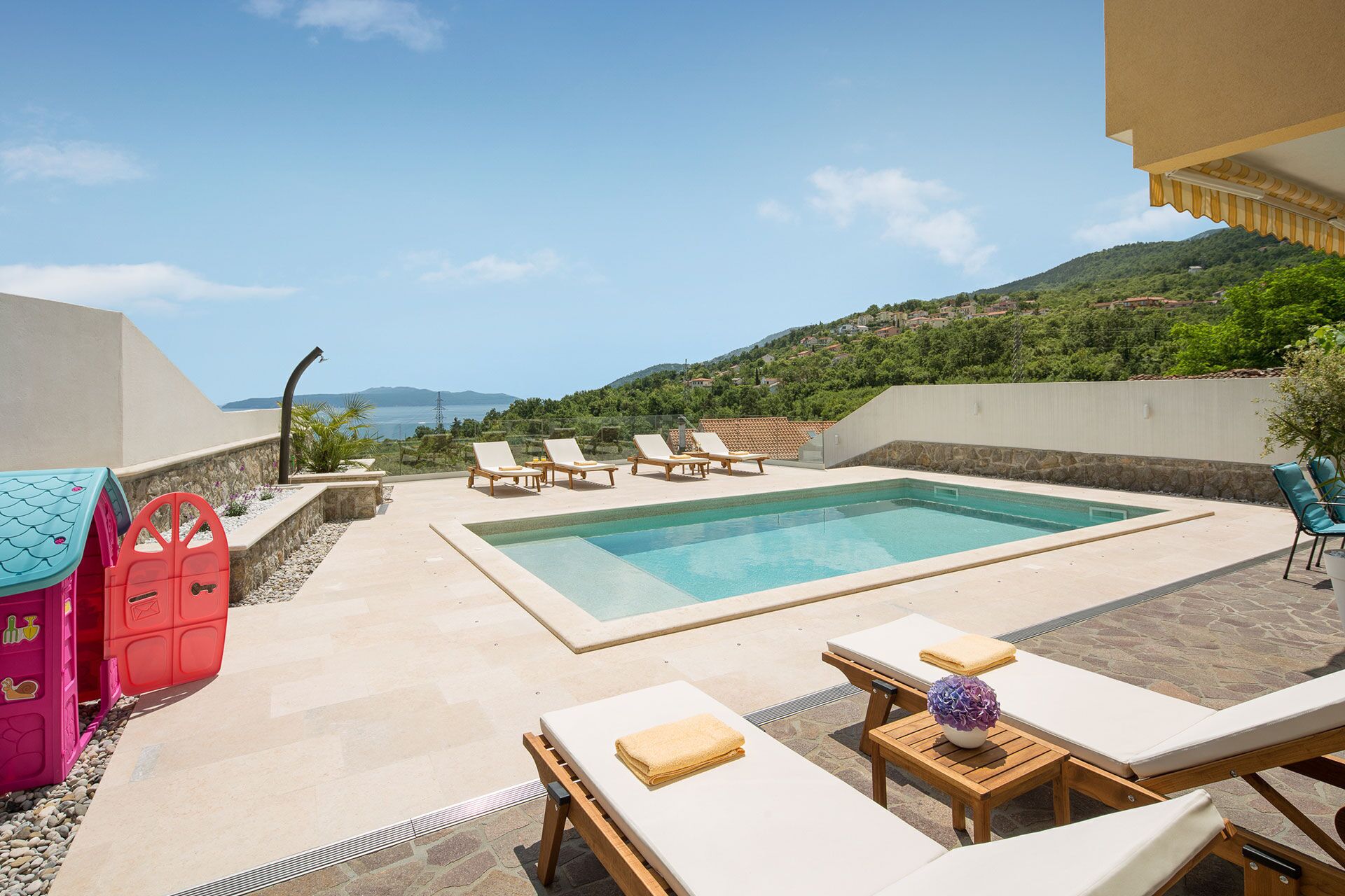 A pool area with lounge chairs, a children's play area, and a view of the sea.