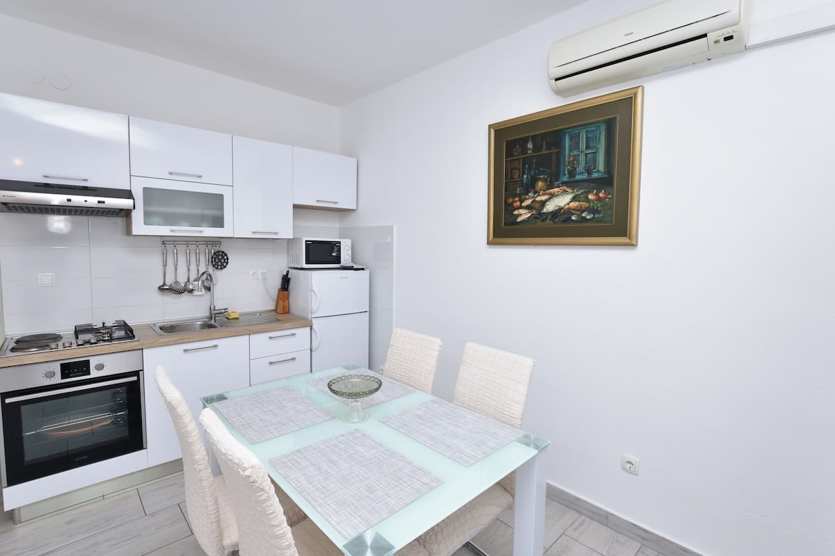 A modern kitchen with white cabinets, a microwave, a stove, and an oven. There is a dining table with chairs and a framed painting on the wall.