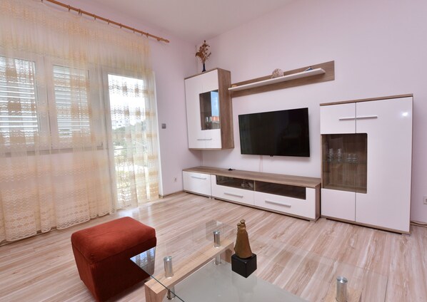 Ein modernes Wohnzimmer mit Flachbildfernseher, Holzkästen, einem Glastisch und einem roten Sessel.