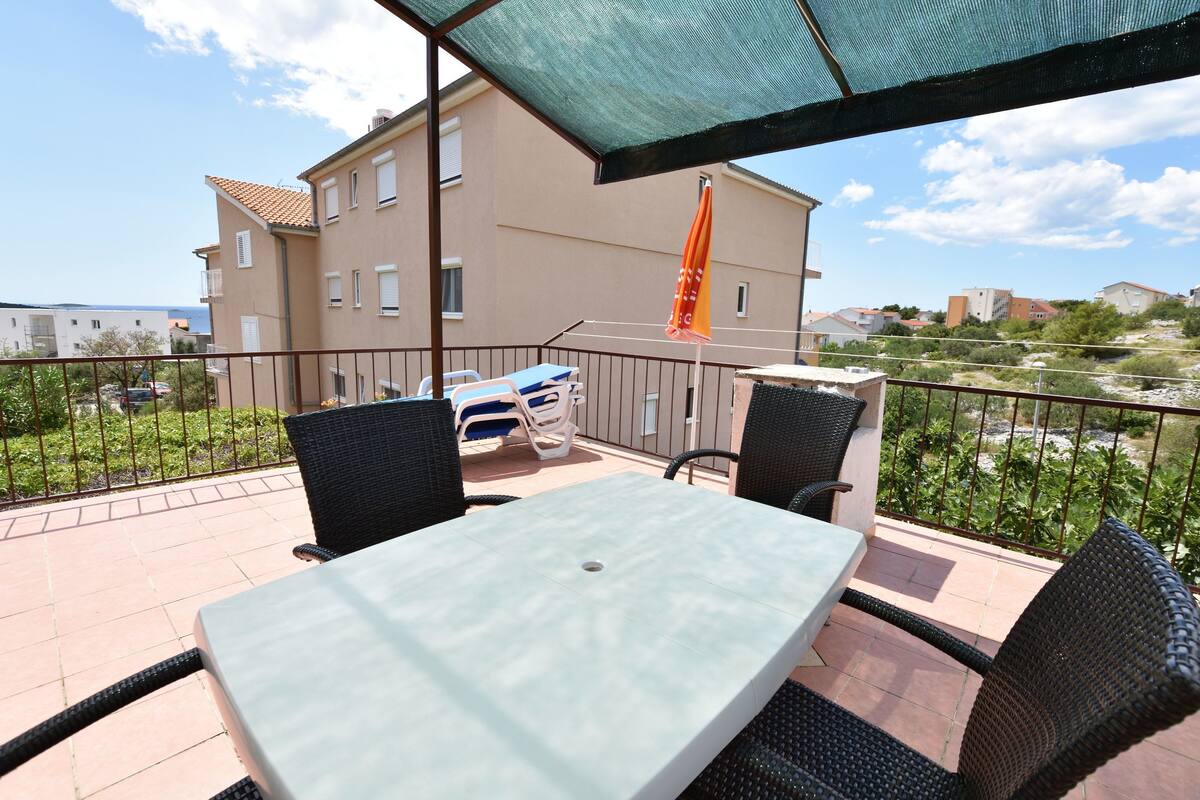 A balcony with a table and chairs, a car parked outside, and a building in the background.