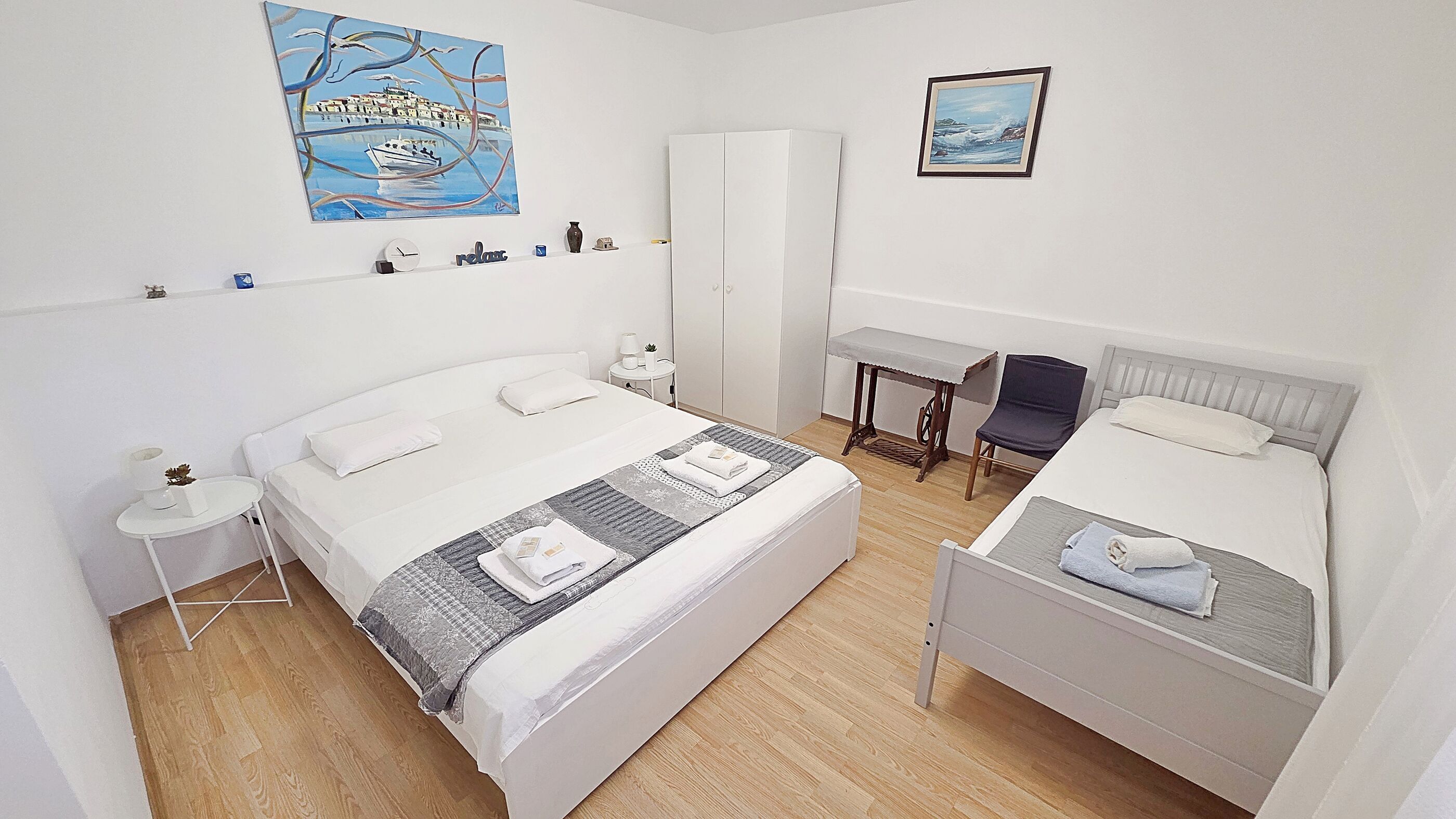 A hotel room with two beds, a desk, a wardrobe, and artwork on the walls.