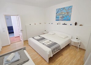 Un dormitorio con una cama, mesitas de noche, un cuadro y vistas a una habitación azul a través de una puerta abierta.