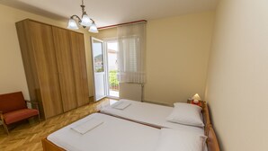 Een slaapkamer met twee bedden, een houten garderobe, een rode stoel en een raam met gordijnen.
