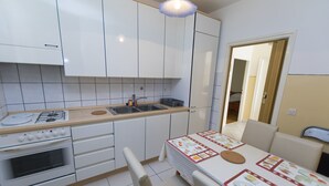 Een kleine keuken met witte kasten, een gasfornuis, een spoelbak en een eettafel met een placemat.