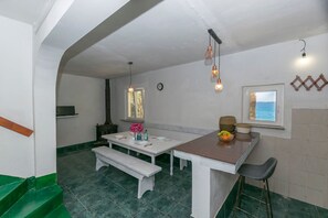 Una cocina con una mesa blanca, un banco y un taburete de bar. Hay lámparas colgantes y una ventana con vista al mar.