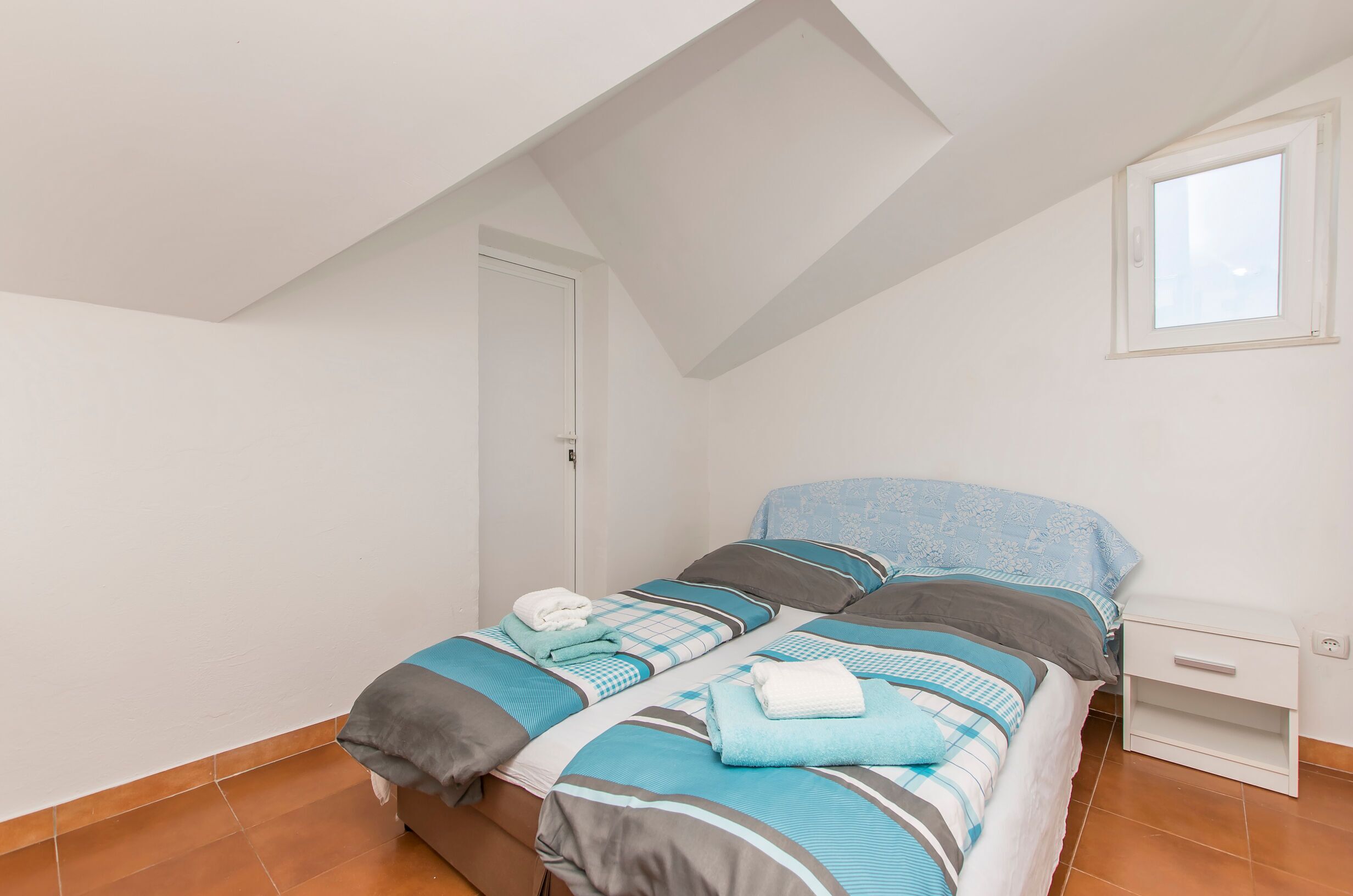 A bedroom with two beds, a skylight, a window, and a white nightstand.