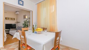 A dining area with a table set for two, a television in the background, and a plant on the table. - Apartment Antonija (Primosten)