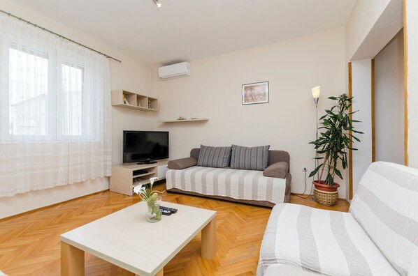 A living room with a sofa, a TV, a coffee table, and a potted plant.