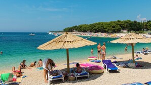 A beach with umbrellas, lounge chairs, and people sunbathing. - Apartment Antonija (Primosten)