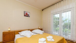 A hotel room with a bed, pillows, a bedside table with a lamp, and a window with curtains. - Apartment Antonija (Primosten)