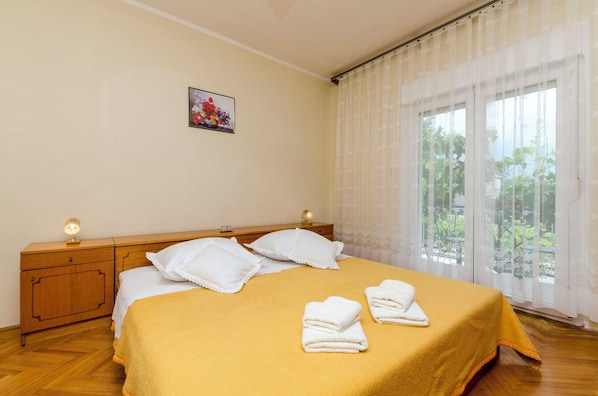 Una camera d'albergo con un letto, cuscini, un comodino con una lampada e una finestra con tende.