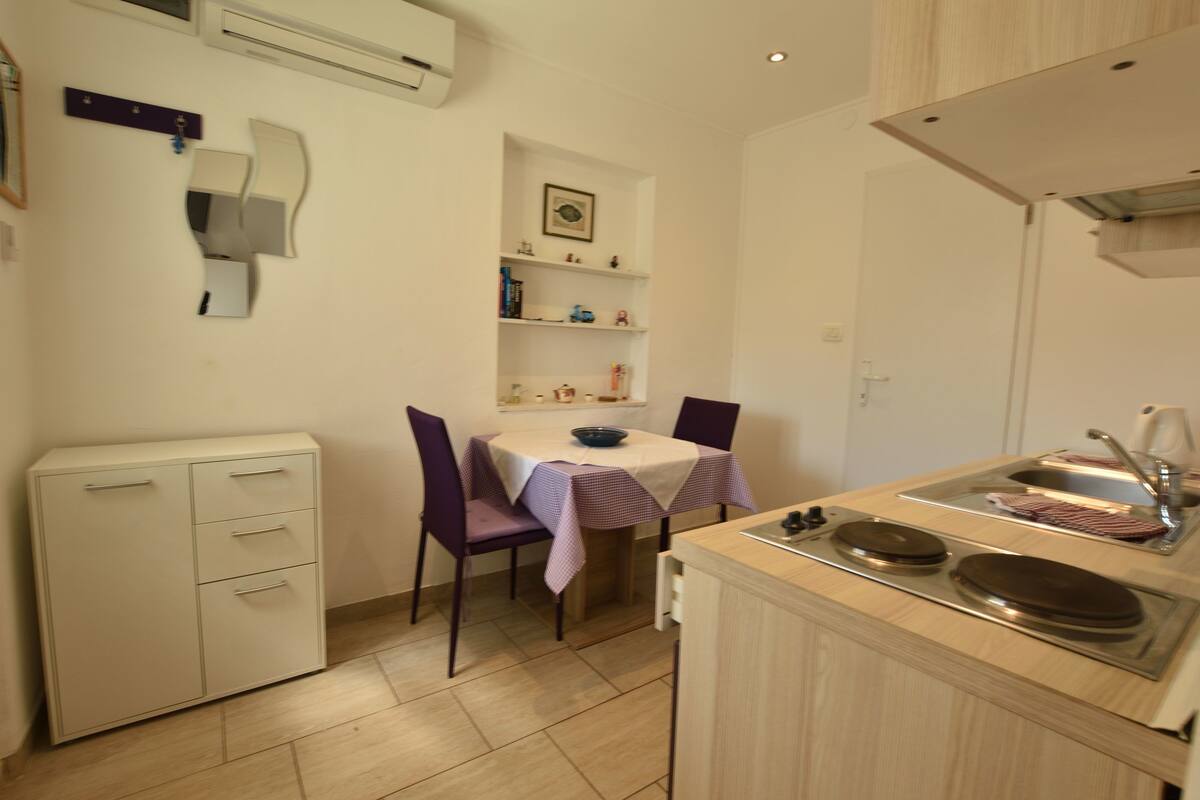 A compact kitchen with a table, chairs, a small cabinet, and a sink.