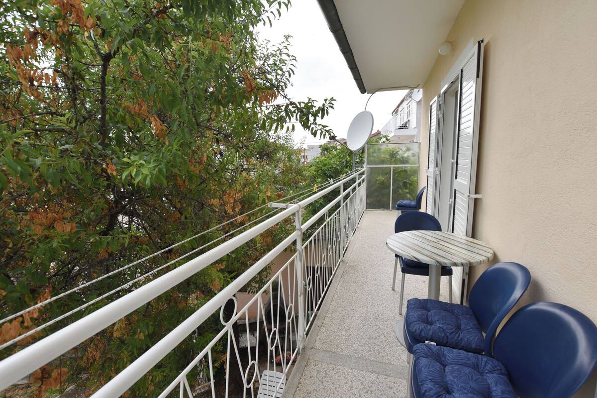 A balcony with a white railing, a table, and blue chairs.