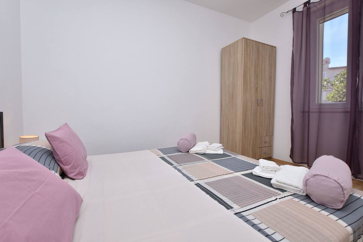 A bedroom with a bed, pillows, a wardrobe, and a window with curtains.