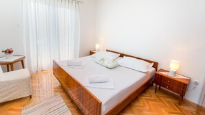 Ein ordentlich eingerichtetes Schlafzimmer mit einem hölzernen Bett, weißen Leinen, einem Nachttisch mit Lampe und einem kleinen runden Tisch mit Blumen in einer Vase.