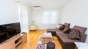 Ein modernes Wohnzimmer mit einer Couch, einem Fernseher und einem kleinen Tisch mit einer Vase.