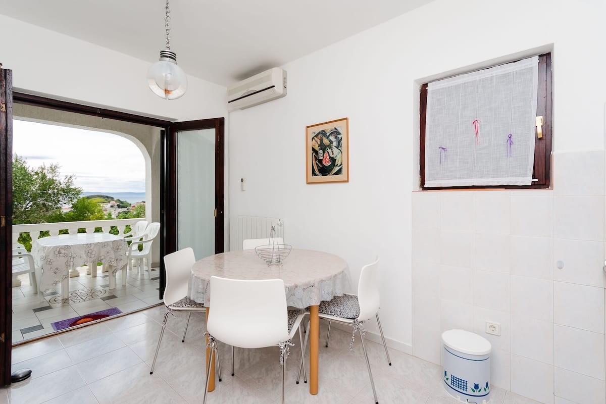 A dining area with a round table, white chairs, and a view through a glass door.