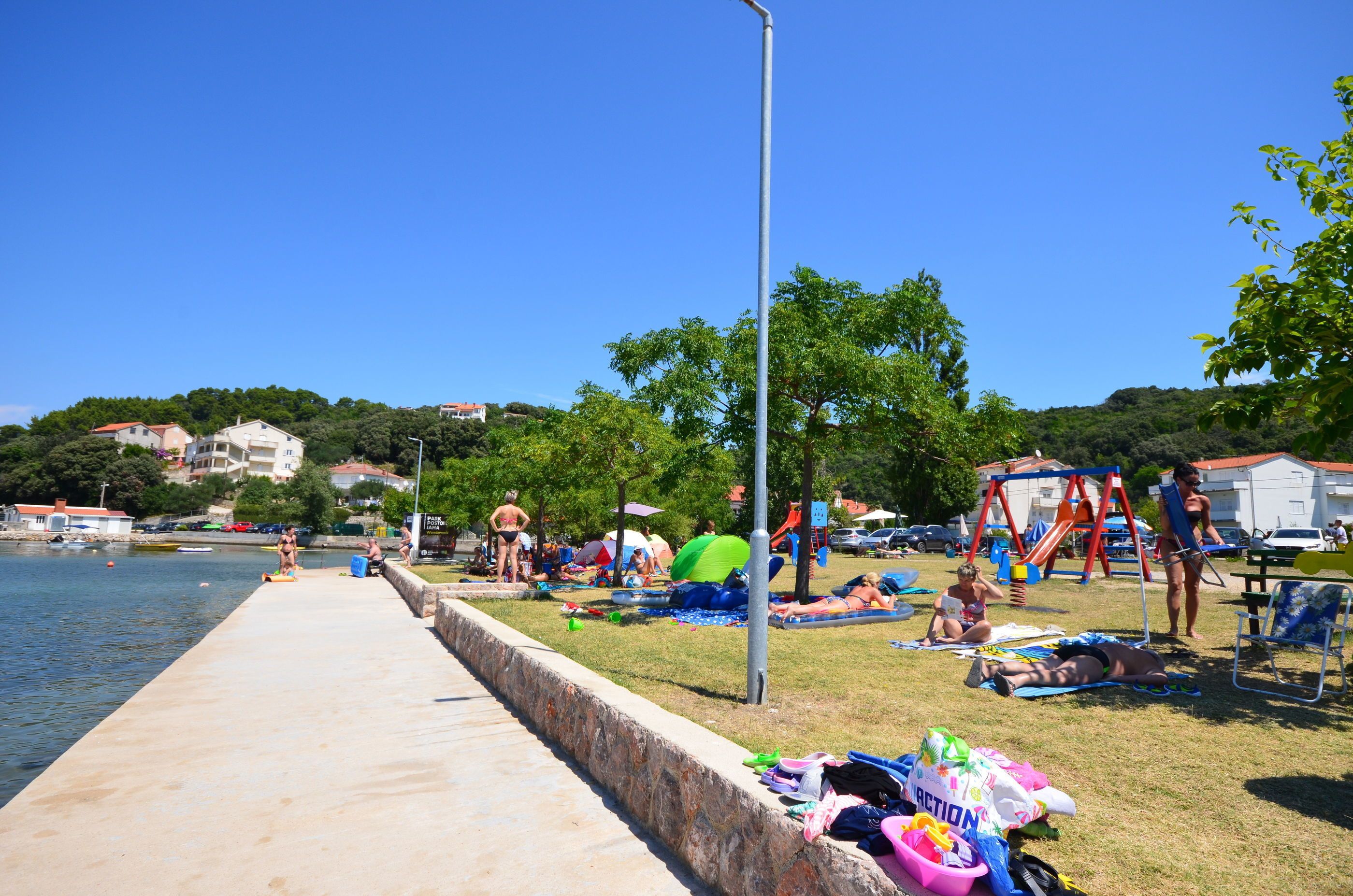 Un parque frente al agua con un paseo de hormigón, mesas de picnic y un parque infantil.