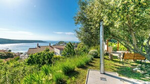 Un parc avec un banc, une sculpture en métal et une vue sur la mer et les maisons.