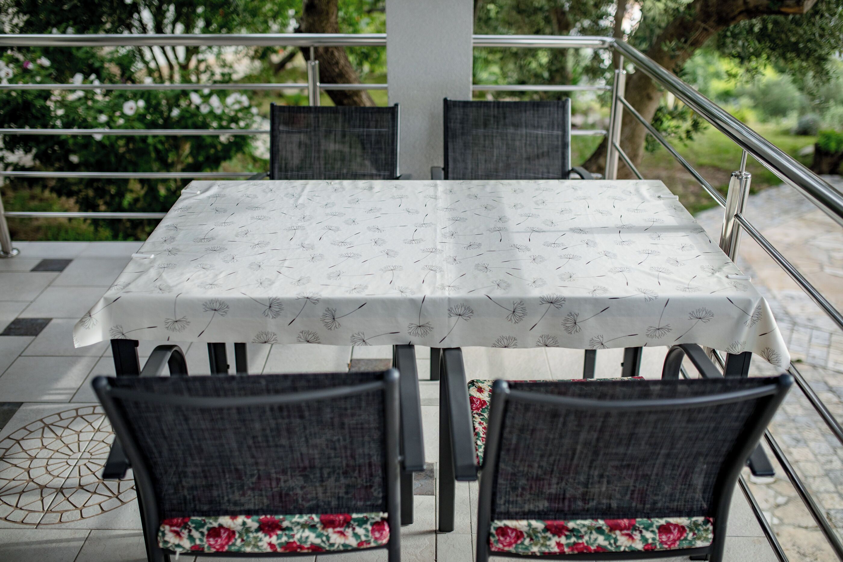 Un tavolo con una tovaglia floreale, quattro sedie con cuscini decorati con motivi floreali e vista sul verde.