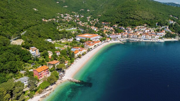 Vista aérea de uma cidade costeira com praia, edifícios e montanhas ao fundo.