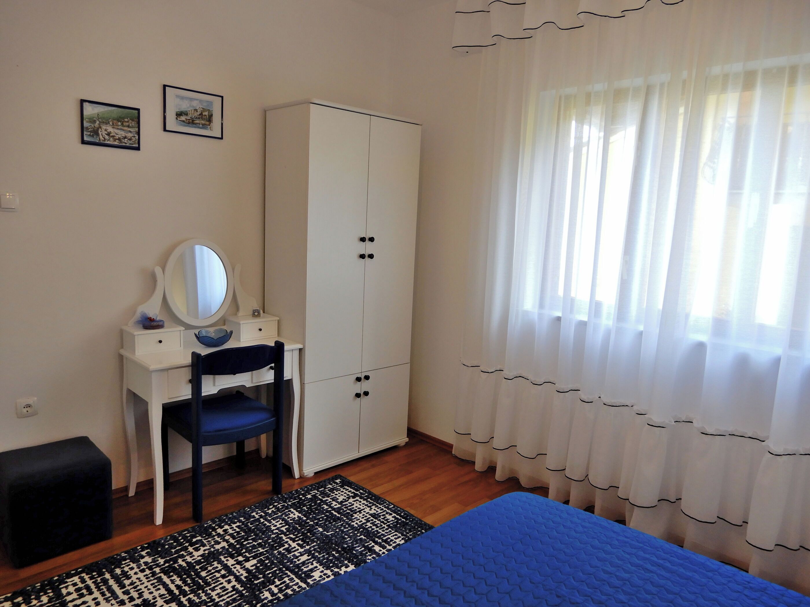 A bedroom with a bed, a desk with a chair, a wardrobe, and a window with curtains.