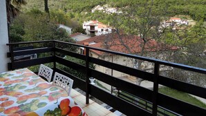 Uma varanda com mesa e cadeiras, com vista para uma colina com edifícios.