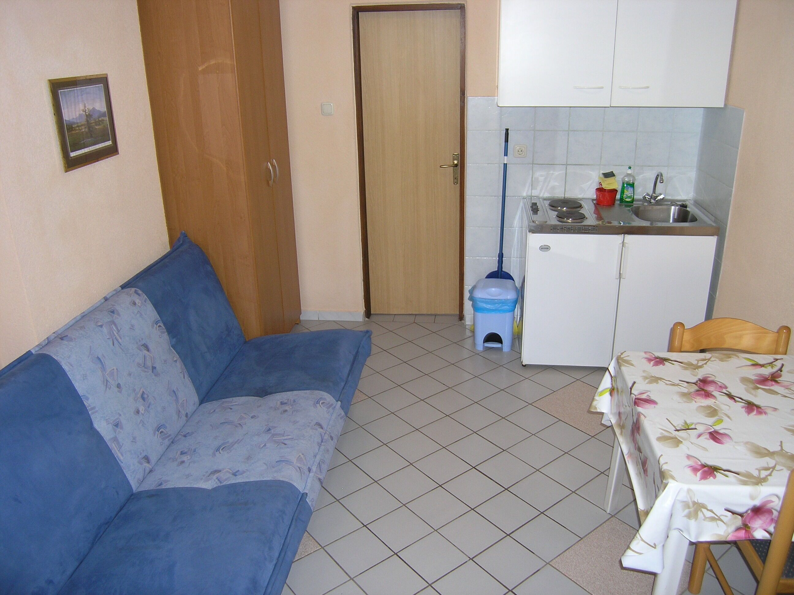 A small, compact living space with a sofa, a dining table, a kitchen area, and a door leading to another room.