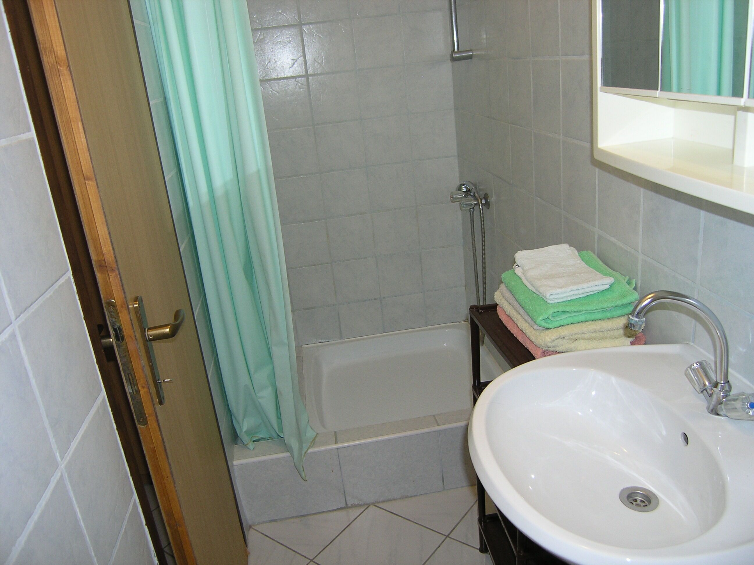 A bathroom with a white sink, a bathtub, and a shower. There is a stack of folded towels on a shelf.