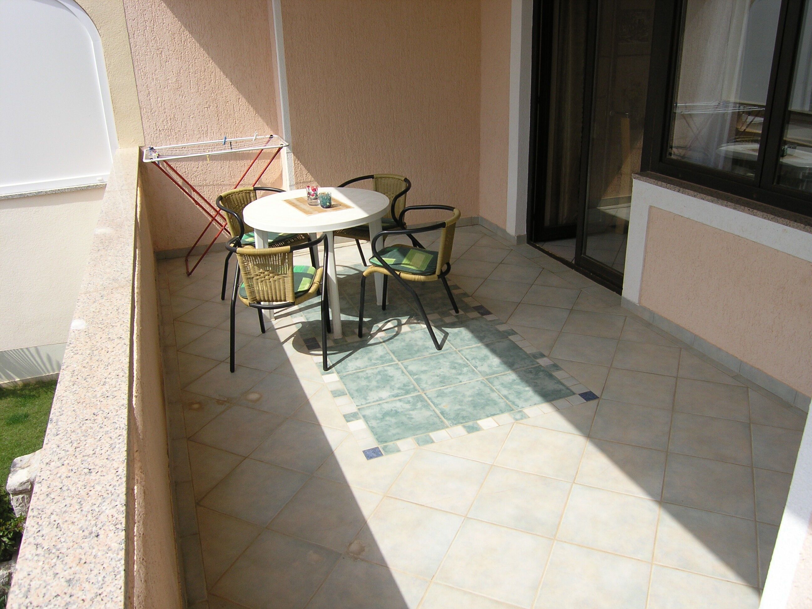 A small patio with a round table and four chairs, a drying rack, and a window with a view.