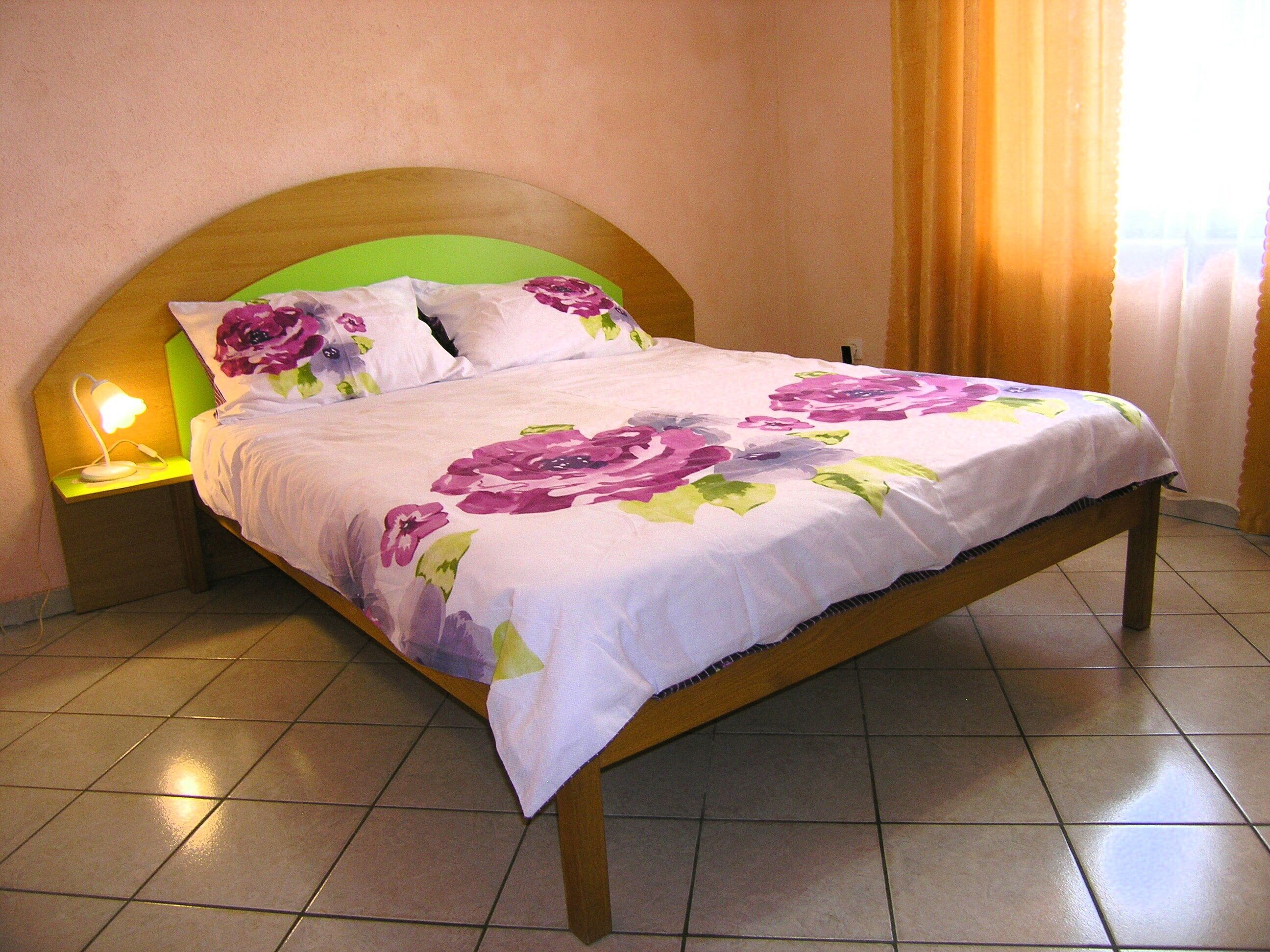 Una cama con colcha estampada, una mesita de noche con lámpara y un cabecero de madera.