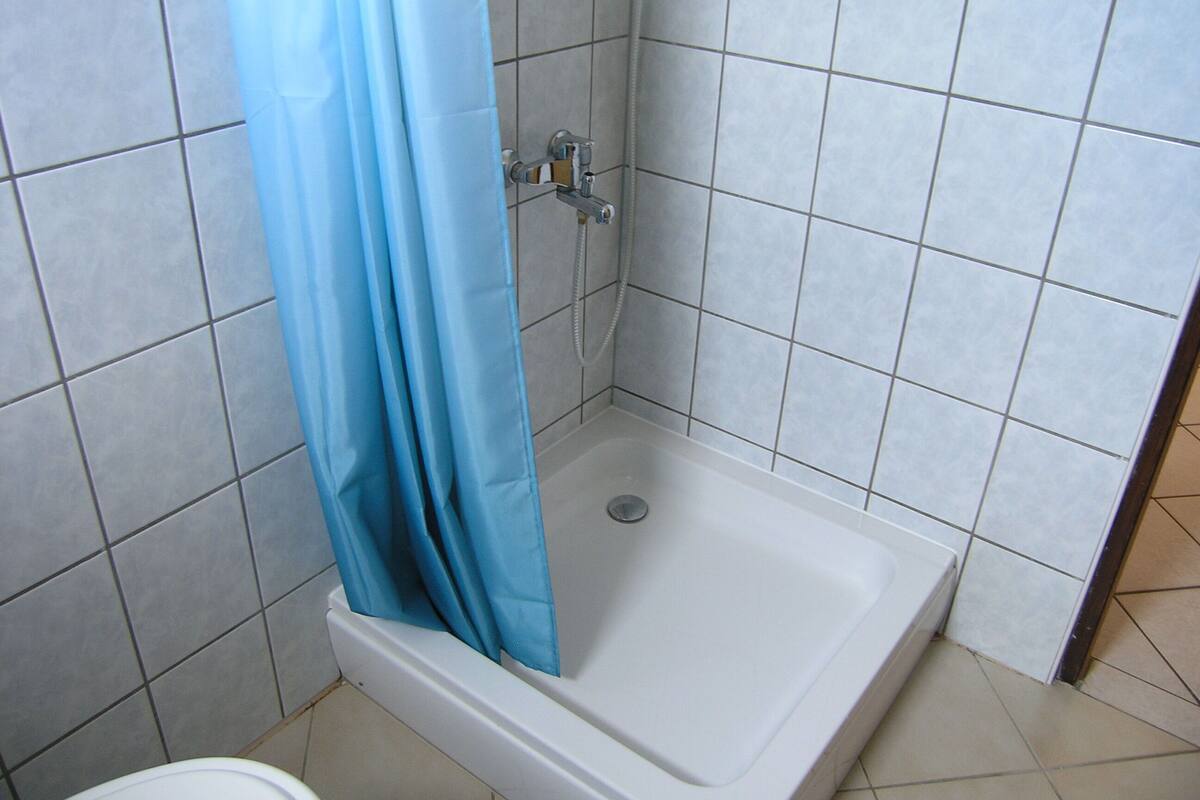 Una doccia con tenda blu, una vasca da bagno bianca e pareti piastrellate.