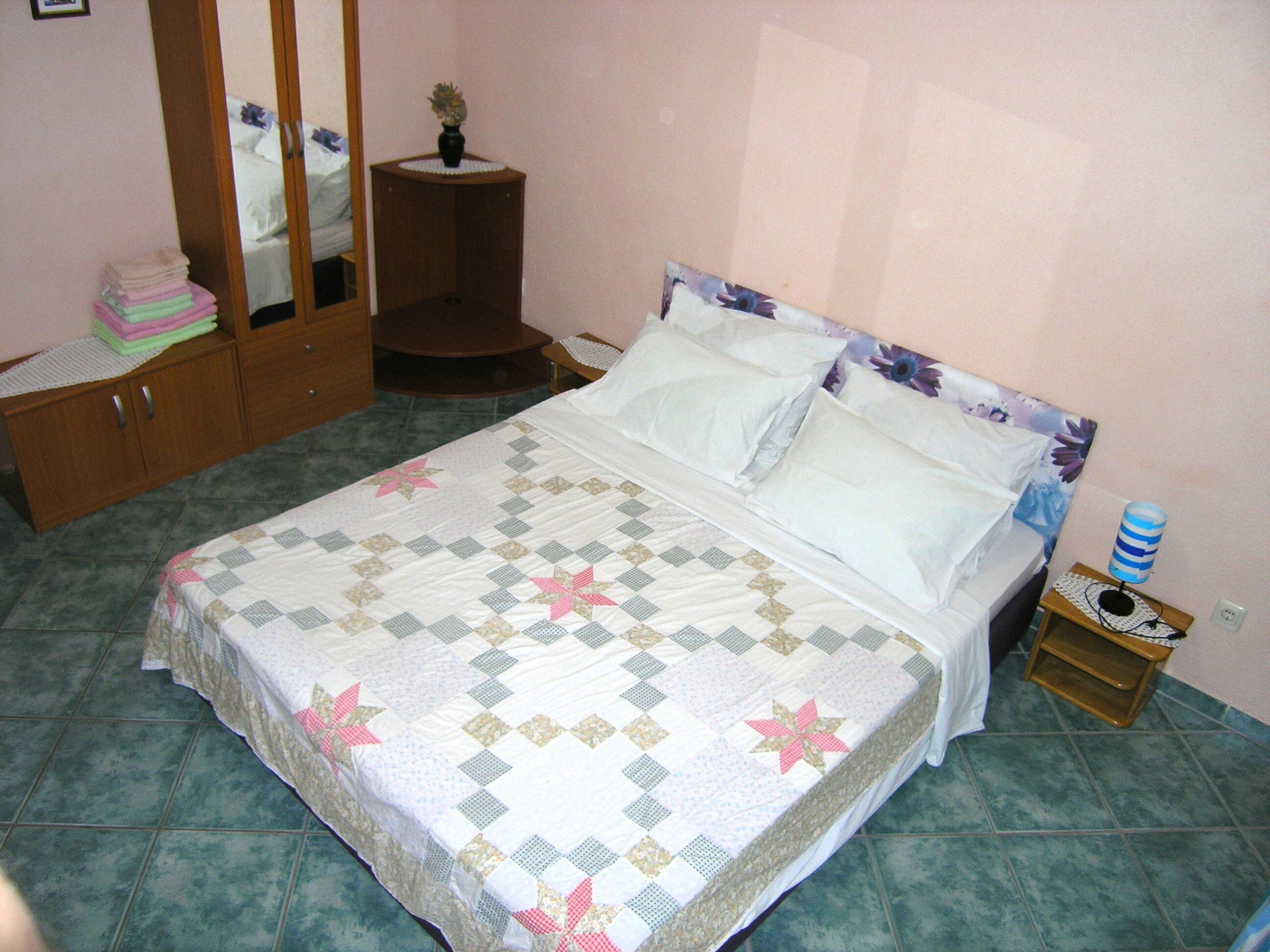 A bedroom with a bed, a wardrobe, a bedside table with a lamp, and a mirror.