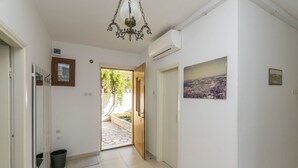 A hallway with a wooden door, a small stool, and a view of an outdoor area with a stone pathway and greenery. - Apartment Linda (Primosten)