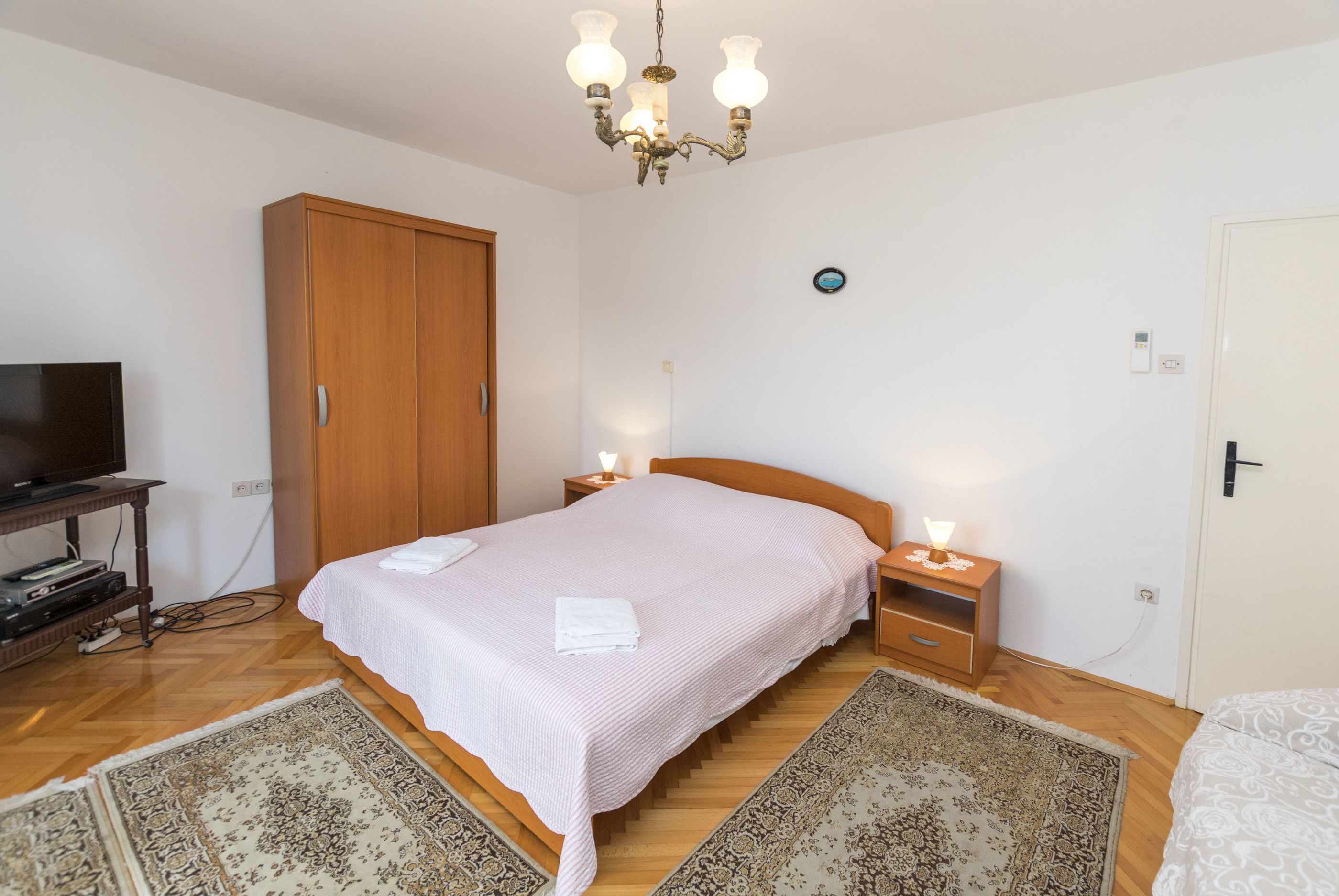 Ein Schlafzimmer mit einem hölzernen Bett, Nachttischen, einem Fernseher und einer Chandelier.