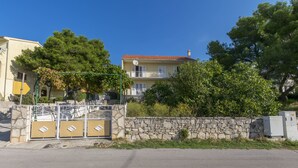 A two-story building with a stone wall and a metal gate. - Apartment Linda (Primosten)