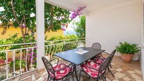 Een balkon met een tafel en stoelen, omringd door planten en uitzicht op groen.
