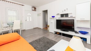Een moderne woonkamer met een flatscreen televisie, witte meubels en een eethoek met een glazen tafel en stoelen.