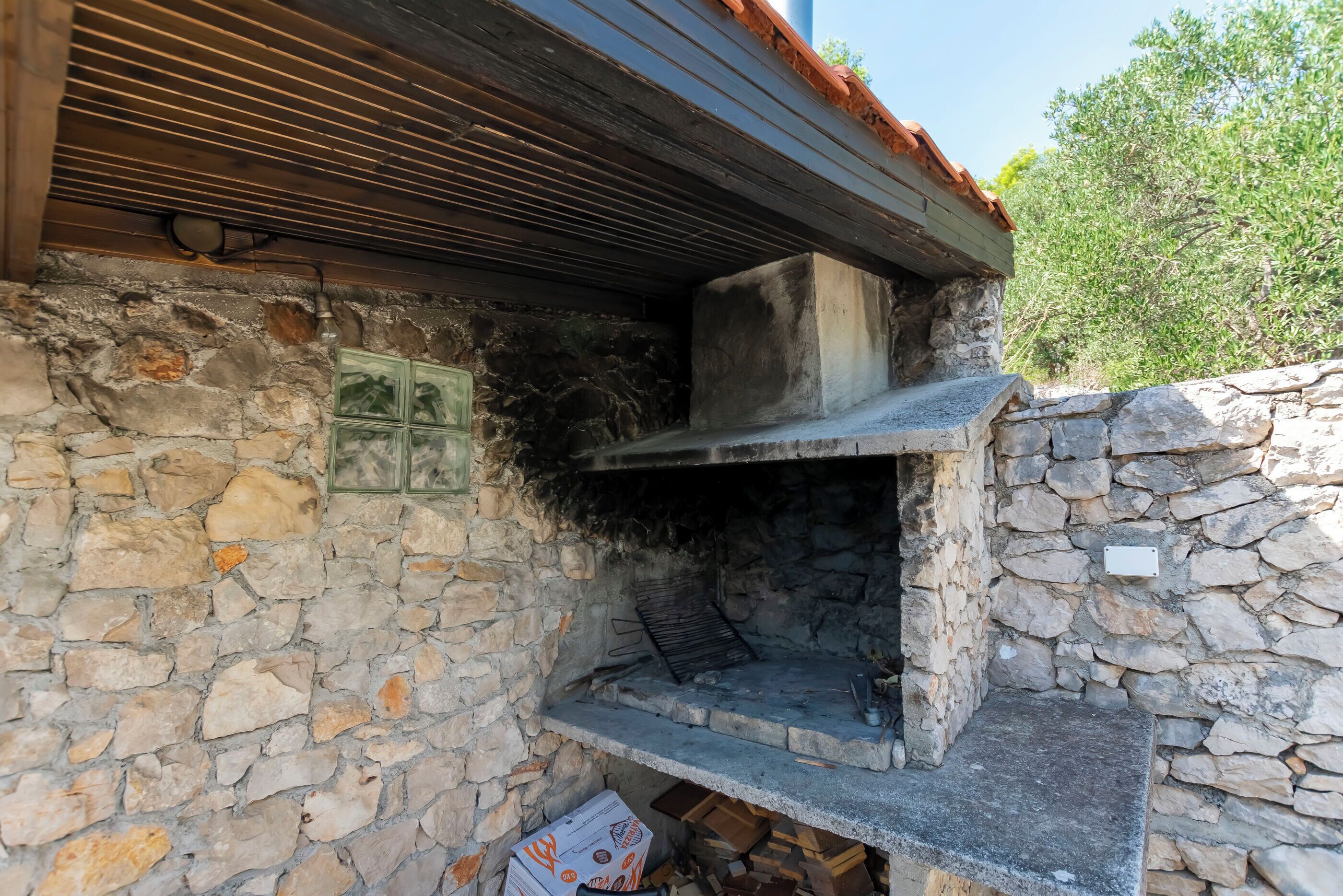 Eine Außenküche aus Stein mit integriertem Grill, Steinmauern und einer rustikalen Holzbalkendecke.