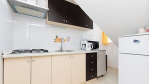 Een moderne keuken met een gasfornuis, een gootsteen en een koffiezetapparaat. Er zijn kasten en een koelkast.
