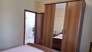 A bedroom with a bed, a wooden wardrobe, a chair, and a bedside table. - Apartments Stana (Zadar)