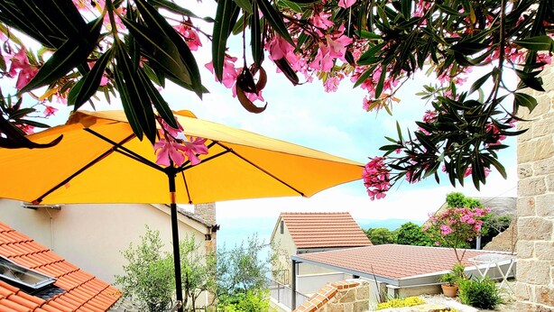 An outdoor seating area with a blue table and chairs, a yellow umbrella, and pink flowers. - House Cottage (Lokva Rogoznica)