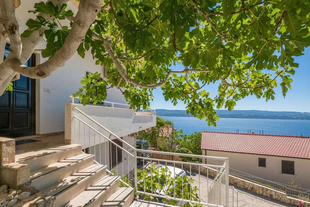 Una scala conduce a un balcone con vista sul mare, con un albero che offre ombra.