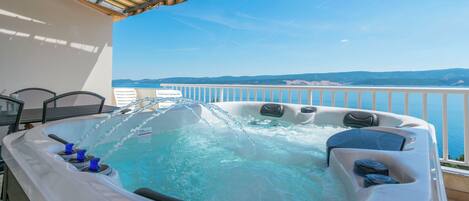 A hot tub with jets, a table with chairs, and a view of the sea.