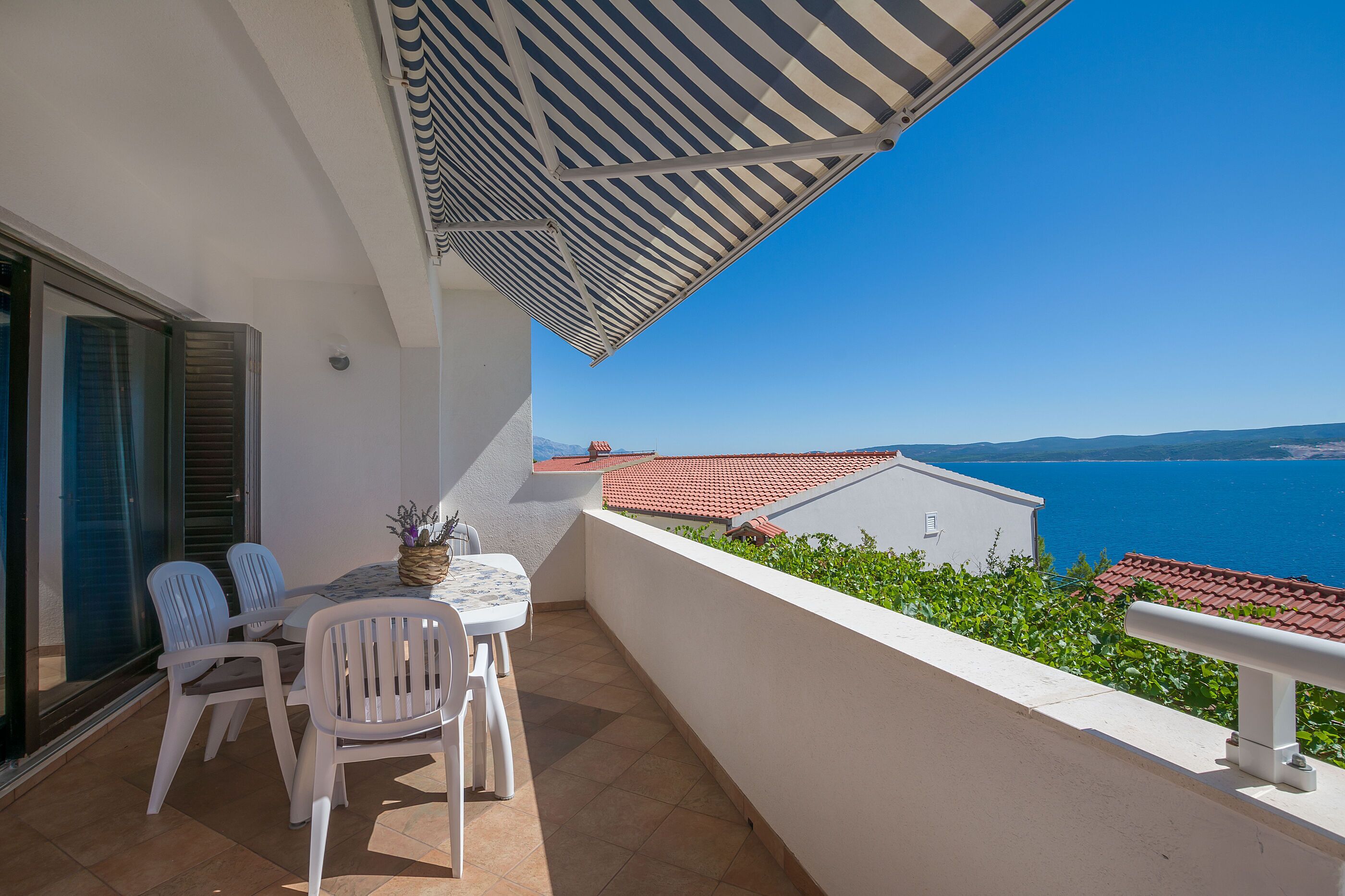A balcony with a table and chairs, overlooking a coastal view with buildings and the sea.